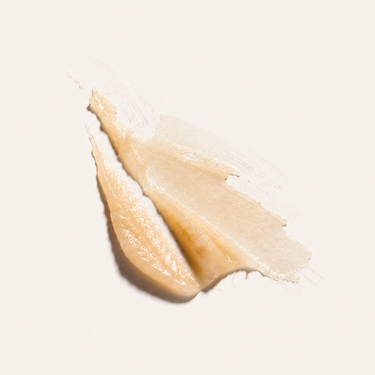 A textured swipe of creamy, semi-translucent beige cosmetic cream or balm on a solid off-white background.